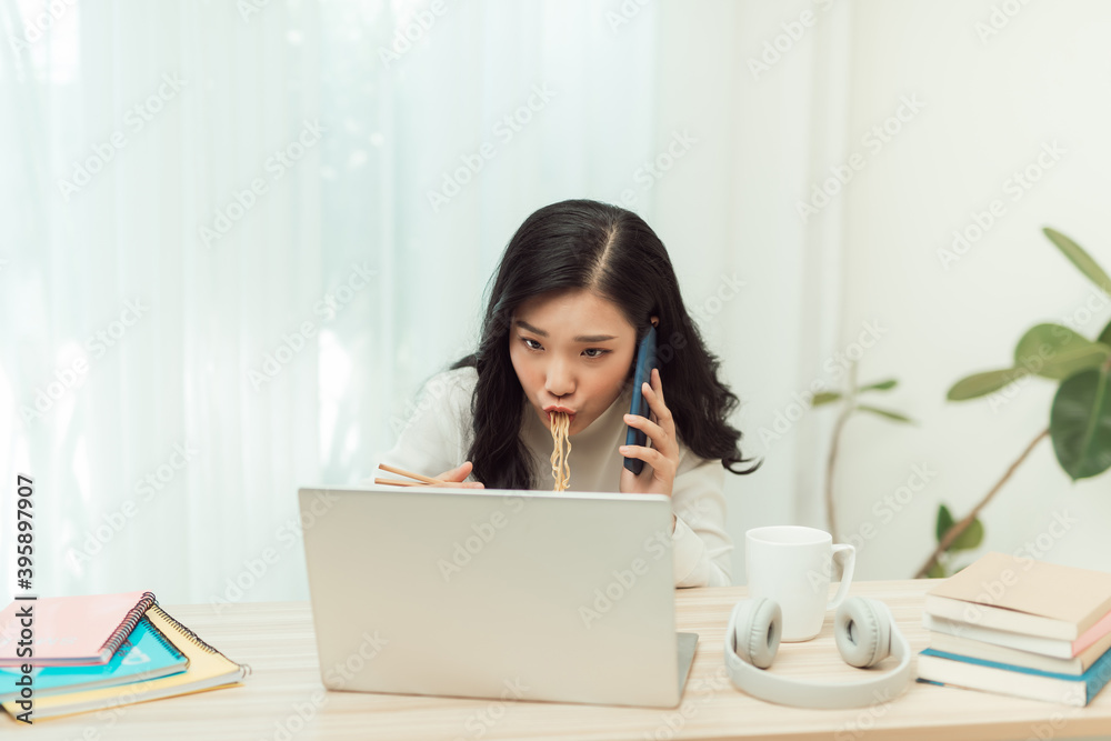 woman eating noodles while working with laptop and cellphone in office woman eating noodles while working with laptop and cellphone in office