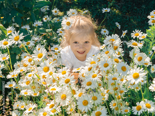 smiling little girl in a white t-shirt sitting in white daisies during the day