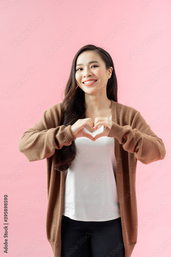 Young woman standing isolated on pink background showing heart shape hand gesture looking camera smiling cheerful Young woman standing isolated on pink background showing heart shape hand gesture looking camera smiling cheerful