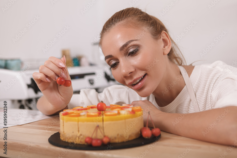 Beautiful cheerful female confectioner garnishing raw vegan cake with cherries Beautiful cheerful female confectioner garnishing raw vegan cake with cherries