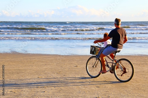 Man with a child riding a bike in the sand of the beach © valdecilima