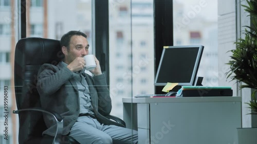 The chief sales Manager talks on the phone while sipping a hot drink and twirling a pencil in his hands, the concept of office work