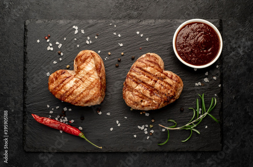 two heart shaped grilled pork steaks with spices for valentines day on stone background. dinner concept for two for valentines day celebration