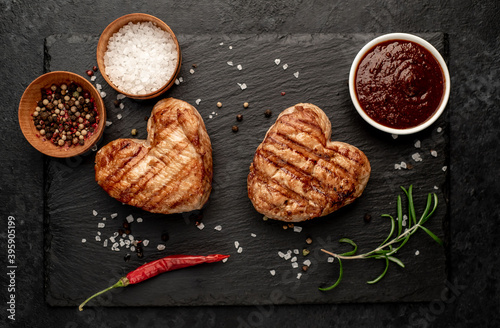 two heart shaped grilled pork steaks with spices for valentines day on stone background. dinner concept for two for valentines day celebration