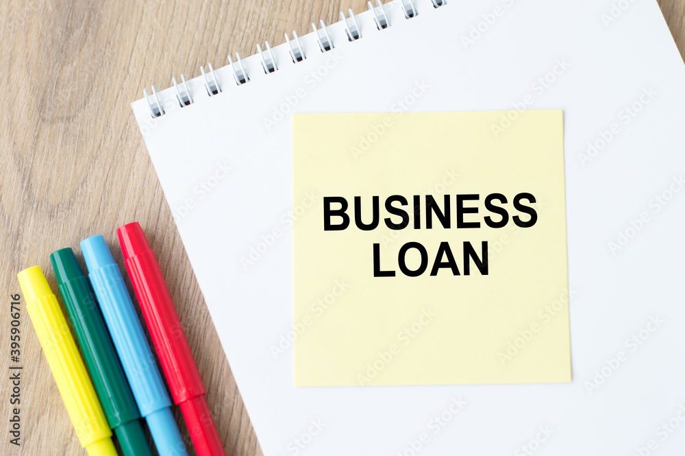 the inscription on the yellow sheet for notes text Business Loan which is attached to the notebook on the table. the inscription on the yellow sheet for notes text Business Loan which is attached to the notebook on the table.