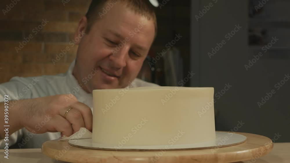 man pastry chef smiles and aligns the cake mold. He wipes off excess cream at the base of the cake with a napkin. Perfectly smooth handmade cake blank. man pastry chef smiles and aligns the cake mold. He wipes off excess cream at the base of the cake with a napkin. Perfectly smooth handmade cake blank.