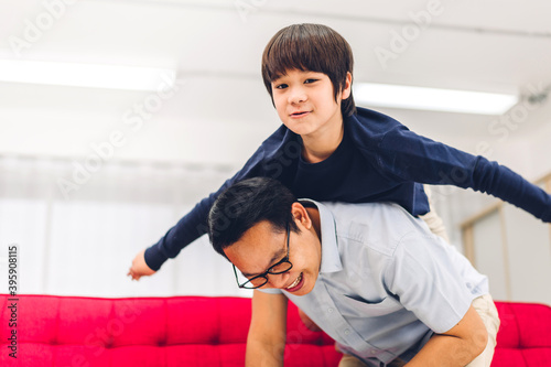 Portrait of enjoy happy love asian family father carrying little asian boy son on back smiling playing superhero and having fun moments good time at home