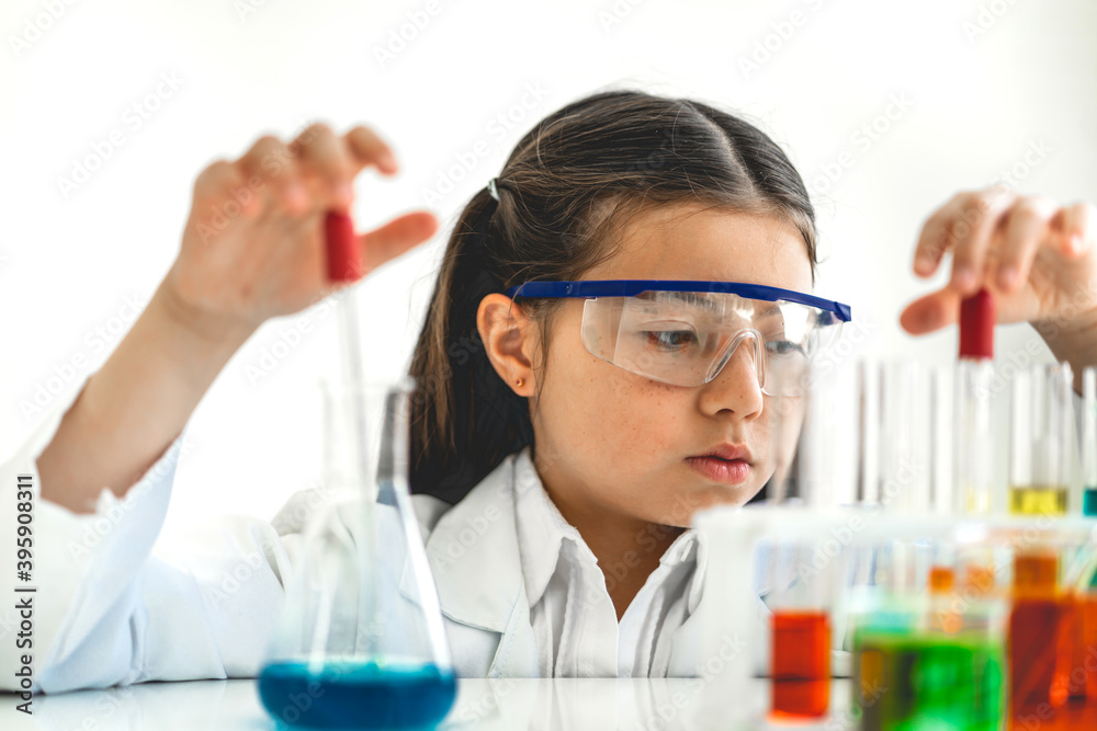 Cute little girl student child learning research and doing a chemical experiment while making analyzing and mixing liquid in glass at science class on the table.Education and science concept