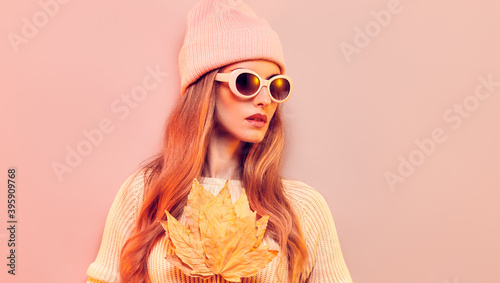 Fashionable hipster woman in Trendy autumn fall outfit, stylish hair, makeup. Blonde model in jumper, fashion jeans having fun smiling. Beautiful girl in autumnal beanie hat with maple leaf