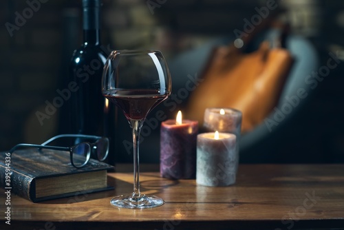 Glass of red wine, open book with candles in the background on wooden table.