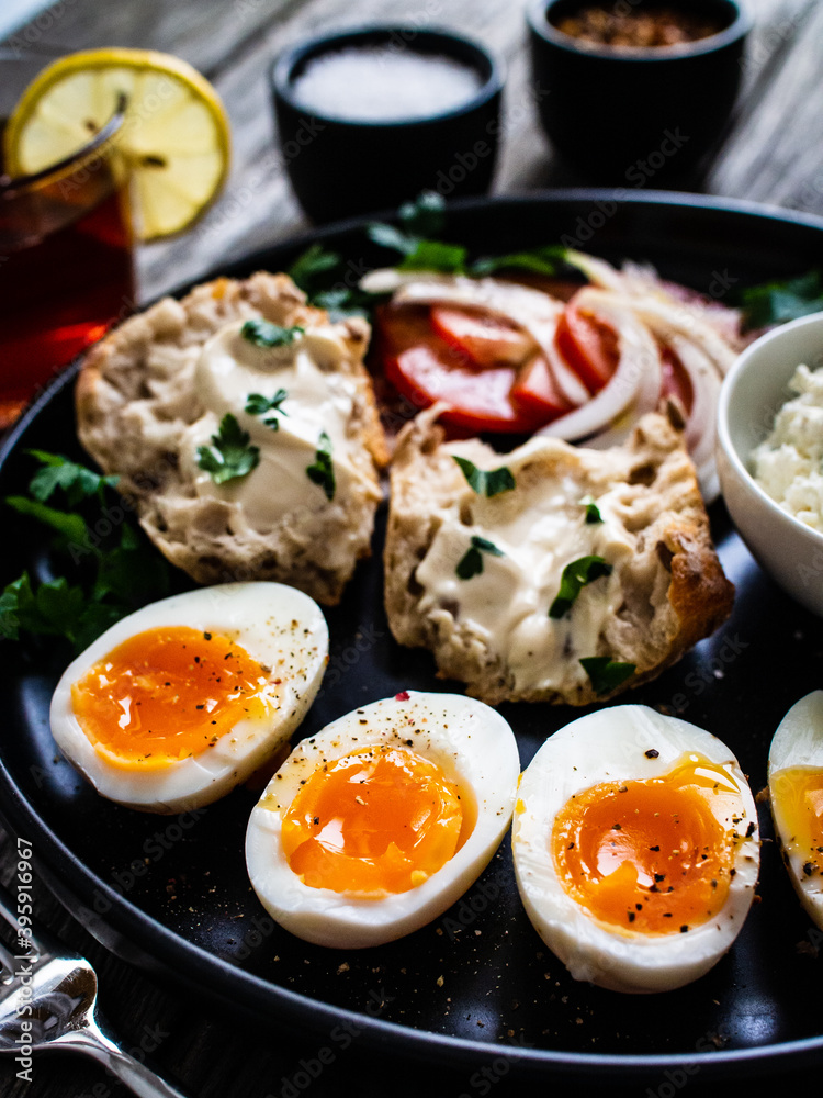 Delicious breakfast - soft boiled eggs with  cottage cheese and vegetables served on black plate on wooden table
