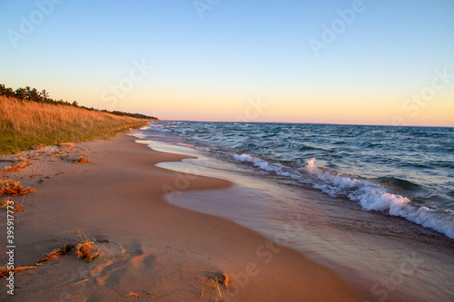 Golden sunset on a wide sandy beach along the coast of Lake Michigan as waves crash onto the shore.
