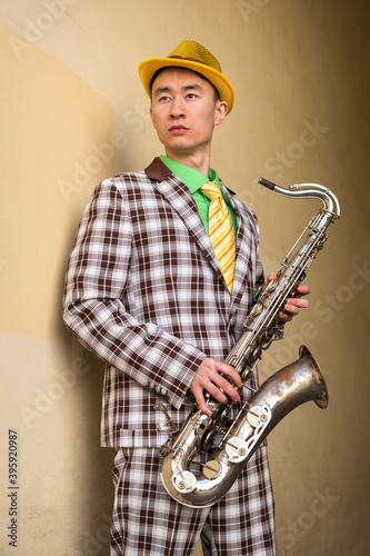Asian guy with saxophone standing against a wall