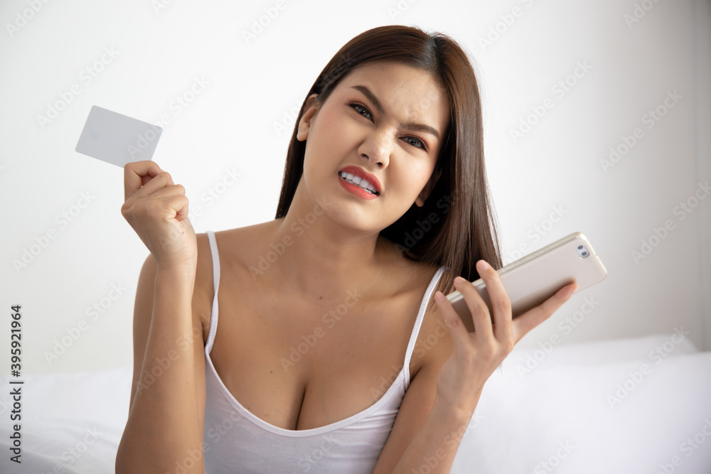Angry upset woman shopping at home with smartphone and credit card; concept of video call, shopping at home, tele shopping app or application, telemedicine VDO call, new normal social distancing Angry upset woman shopping at home with smartphone and credit card; concept of video call, shopping at home, tele shopping app or application, telemedicine VDO call, new normal social distancing