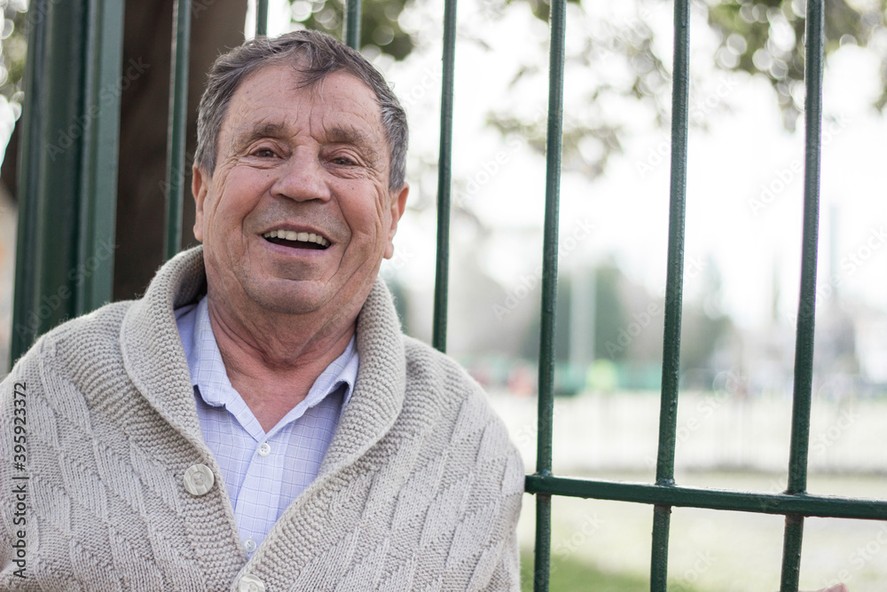 Portrait of happy senior man smiling, in the public park, outdoors. Old man relaxing outdoors and looking at camera. Portrait of elderly man enjoying retirement