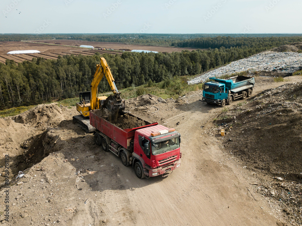 Construction works. Earthmoving at open pit mining. Heavy equipment. Excavator loads ground in red truck. Construction works. Earthmoving at open pit mining. Heavy equipment. Excavator loads ground in red truck.