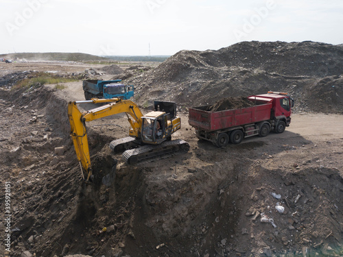 Digger and trucks on excavation pit. Stony soil. Heap of sand. Construction site. Heavy equipment.