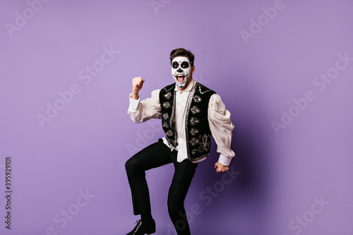 Happy guy is dancing victory dance and shouting joyfully. Full-length portrait of man with painted face