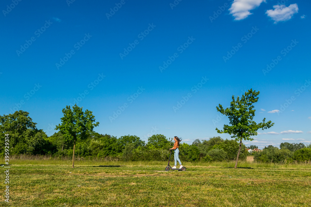 A young woman is driving on an electric scooter through the park A young woman is driving on an electric scooter through the park