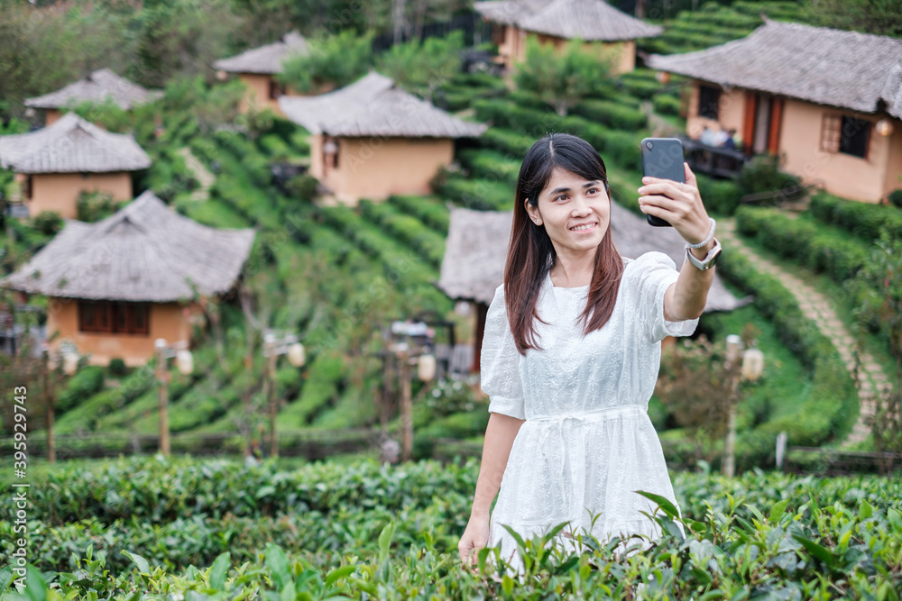 Happy tourist woman in white dress taking photo by mobile smartphone in beautiful Tea garden.Traveler visiting in Ban Rak Thai village, Mae Hong Son, Thailand. travel, vacation and holiday concept Happy tourist woman in white dress taking photo by mobile smartphone in beautiful Tea garden.Traveler visiting in Ban Rak Thai village, Mae Hong Son, Thailand. travel, vacation and holiday concept