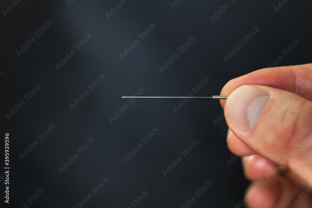 Closeup of an acupuncture needle being held between fingertips Closeup of an acupuncture needle being held between fingertips