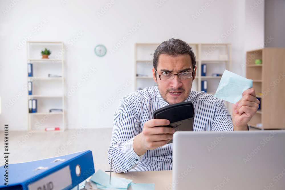 Young male bookkeeper calculating tax payments in the office Young male bookkeeper calculating tax payments in the office