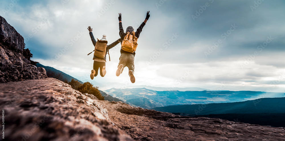 Successful hikers jumping on the top of the mountain - Happy couple with backpack enjoying life at sunset - obrazy, fototapety, plakaty 