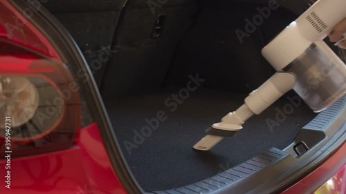 asian man using handheld vacuum cleaning dust from car back storage.