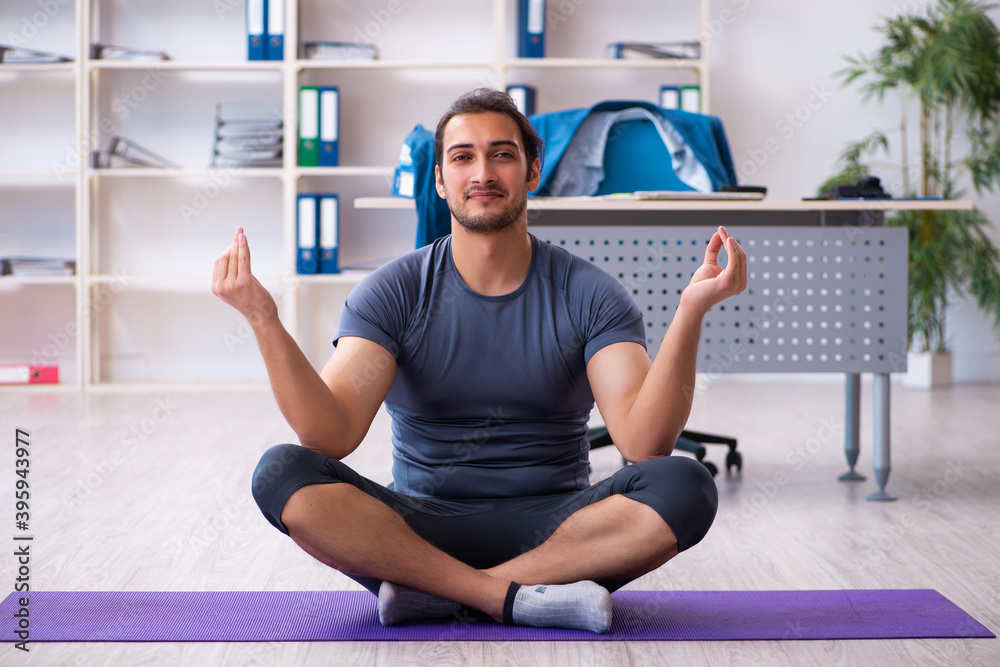 Fototapeta premium Young handsome employee doing sport exercises in the office