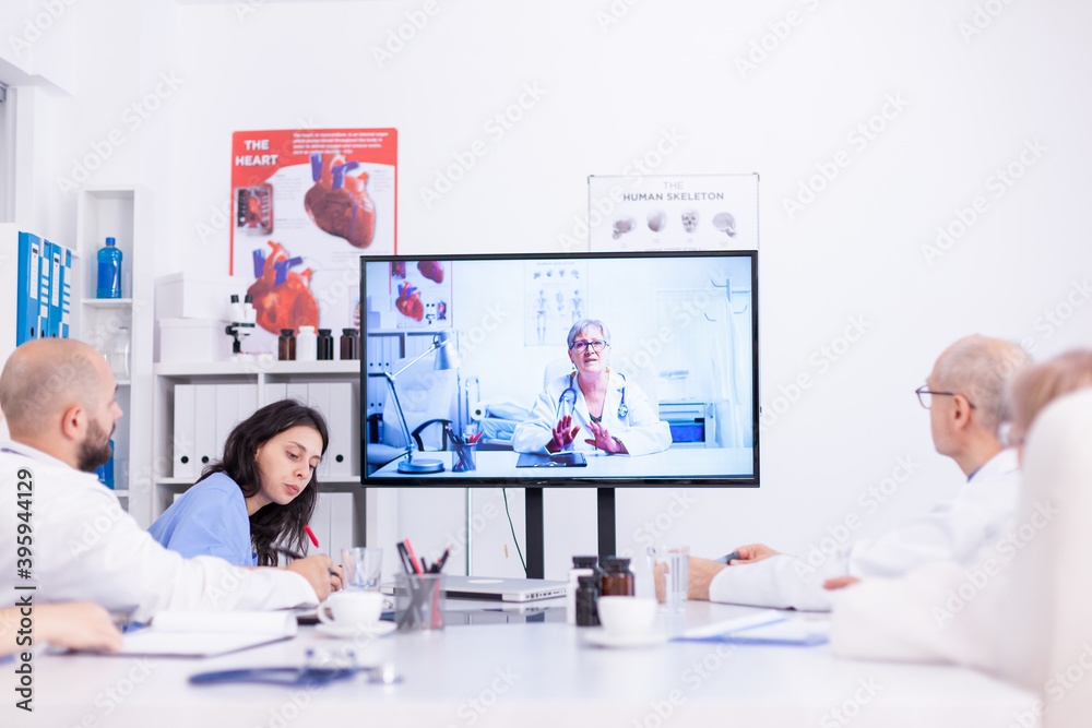 Group of doctors discussing with expert during video conference from hospital meeting room. Medicine staff using internet during online meeting with expert doctor for expertise. Group of doctors discussing with expert during video conference from hospital meeting room. Medicine staff using internet during online meeting with expert doctor for expertise.