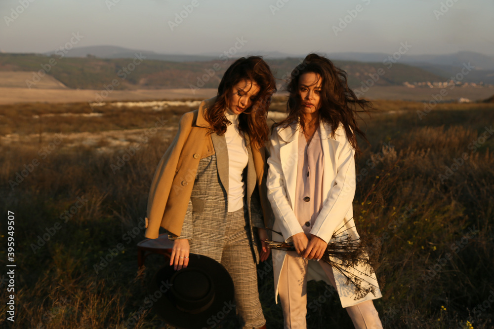 two beautiful women with dark hair in elegant clothes posing in autumn field