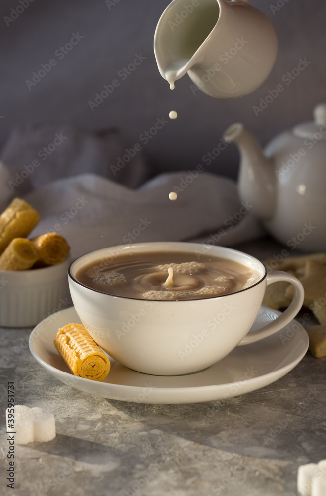 Milk from the milk jug drips into a white mug of tea. the water in the Cup ripples with drops Milk from the milk jug drips into a white mug of tea. the water in the Cup ripples with drops