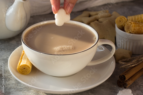 Fotografi A woman's hand puts a lump of sugar in a white mug of tea