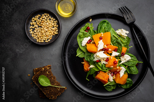 Salad with roasted pumpkin, cheese, spinach, Pine nuts and seasonings on dark background, top view