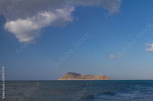 sea and the waves break on the rock and in the background is a mountain and clouds and a blue sky during the day