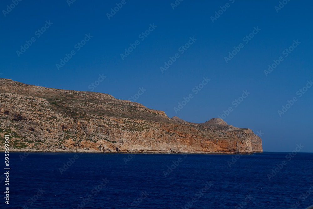 sea and the waves break on the rock and in the background is a mountain and clouds and a blue sky during the day
