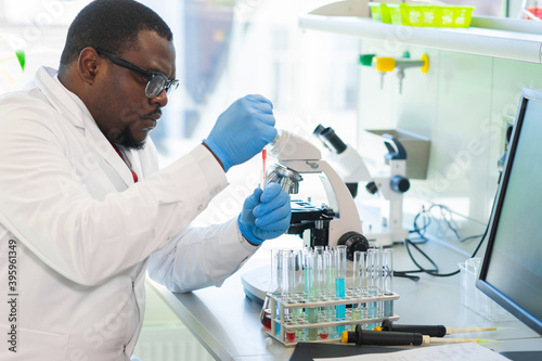 African-american man working in lab. Scientist doctor making medical research. Laboratory tools: microscope, test tubes, equipment. Biotechnology, chemistry, science, experiments and healthcare.
