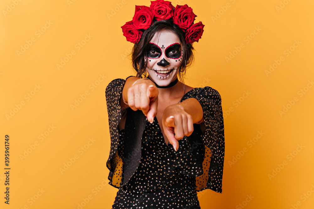 Active cheerful brunette points fingers into camera. Portrait of smiling European model with face art for Halloween