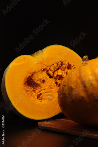 Vertical photo of half a pumpkin with orange flesh. Second part on the right. The background is black, with a wooden Board at the bottom. Transparent drops of juice are visible on the cut. photo