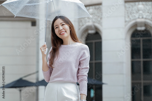 Young Asian woman smile and holding a transparent umbrella under the rain in the city