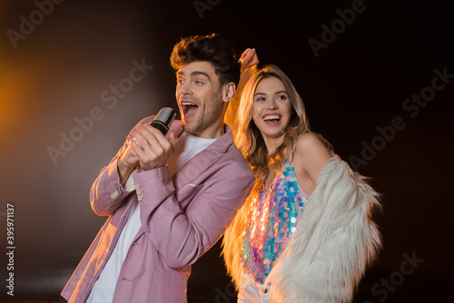 man singing while holding microphone near blonde woman on black