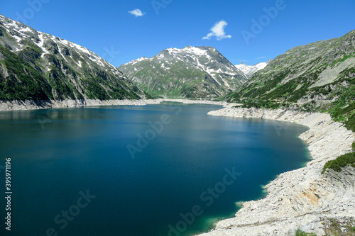 Dam in Austrian Alps. The artificial lake stretches over a vast territory  shining with navy blue color. The dam is surrounded by high mountains. In the back there is a glacier. Controlling the nature
