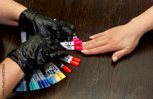 girl chooses color of nail polish for manicure in beauty salon using plastic samples