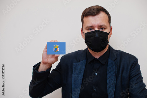 Spanish man wear black formal and protect face mask, hold Melilla flag card isolated on white background. Spain autonomous communities coronavirus Covid concept.