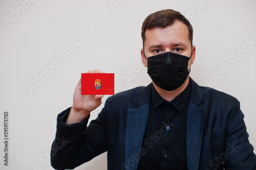 Spanish man wear black formal and protect face mask, hold Avila flag card isolated on white background. Spain provinces coronavirus Covid concept.