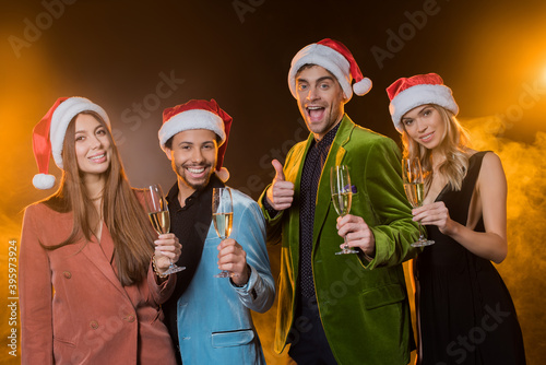  multicultural friends in santa hats holding glasses with champagne on black