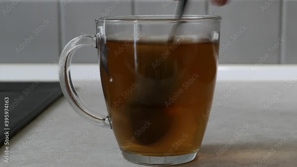 Tea bag mixed with a spoon in a transparent cup filled with water. Background blurred voluntarily. Tea bag mixed with a spoon in a transparent cup filled with water. Background blurred voluntarily.
