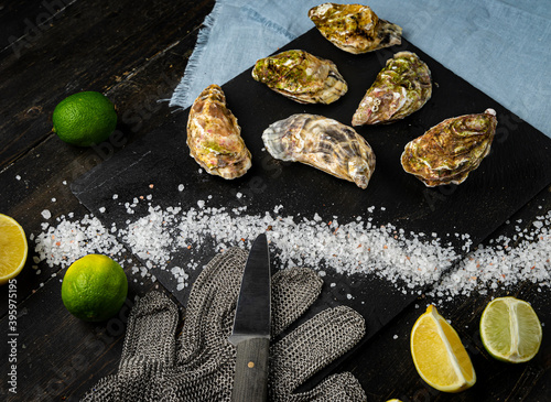 Fresh oysters on a black stone background. Top view. Oyster dinner in restaurant. Dark background. Seafood, Gourmet food. Oyster glove, oyster opening knife 