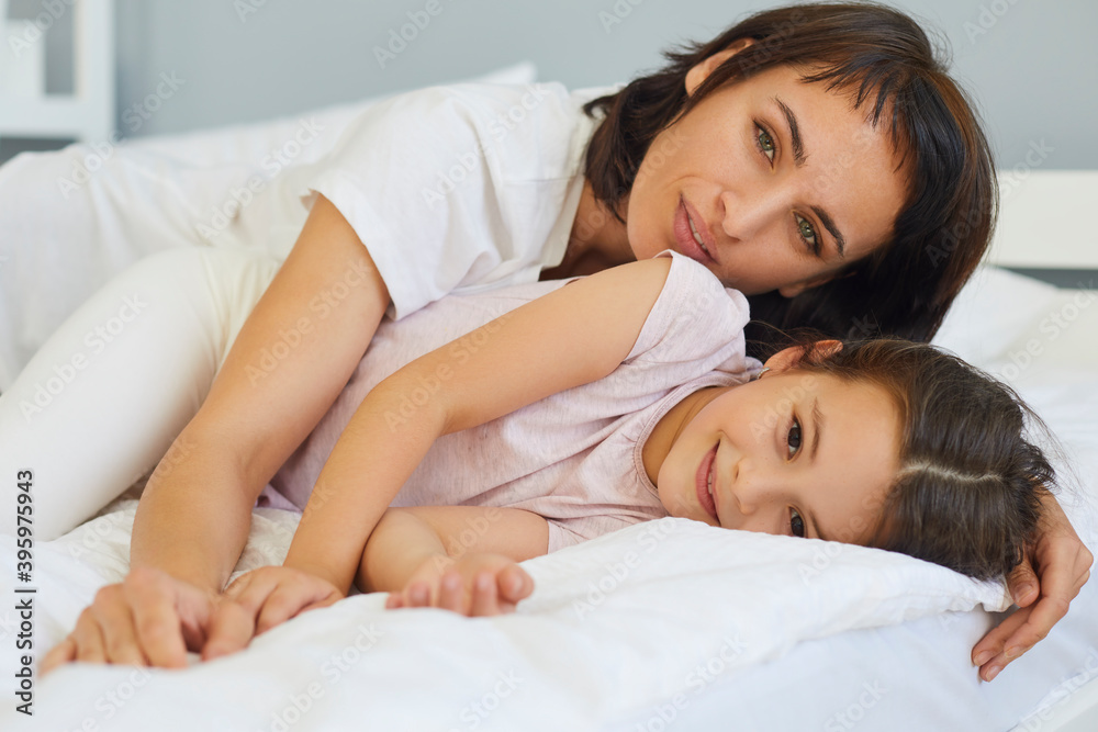 Young mother is playing and hugging with her little daughter on the bed in the bedroom. Young mother is playing and hugging with her little daughter on the bed in the bedroom.