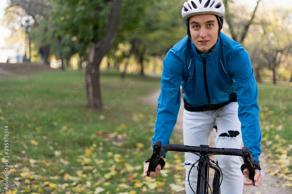 Obraz premium Portrait of a young sporty man who rides a bicycle through the park on a bicycle road. He has a safety helmet and jacket.